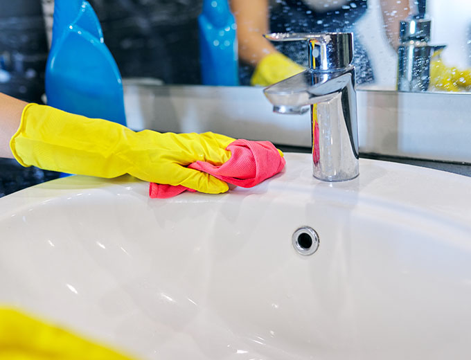 person wearing yellow gloves cleaning a sink with a pink cloth reflecting the importance of cleanliness in two-minute tasks