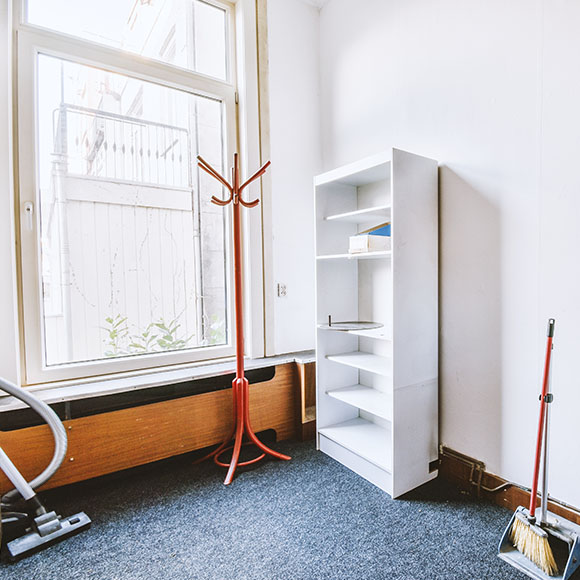 bright room with a white bookshelf red coat rack and cleaning supplies in the corner showcasing minimalistic interior design with three elements
