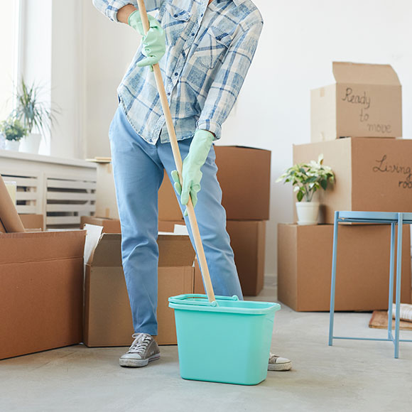 person cleaning with a mop in a room filled with cardboard boxes and a teal bucket representing moving and organization 3 tasks to complete